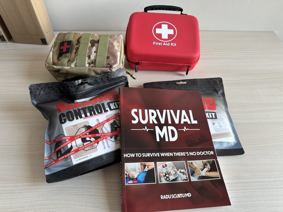 The Survival MD book next to emergency supplies: water, food, a flashlight and a first aid kit