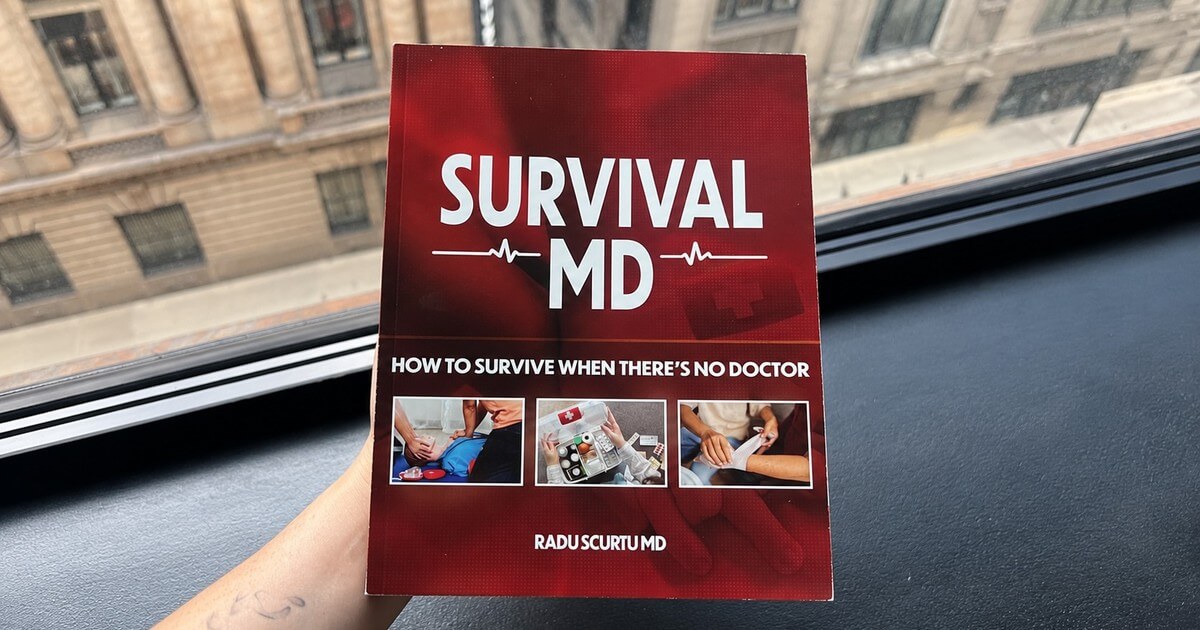 A hand holding up the printed Survival MD book by Dr. Radu Scurtu by a window