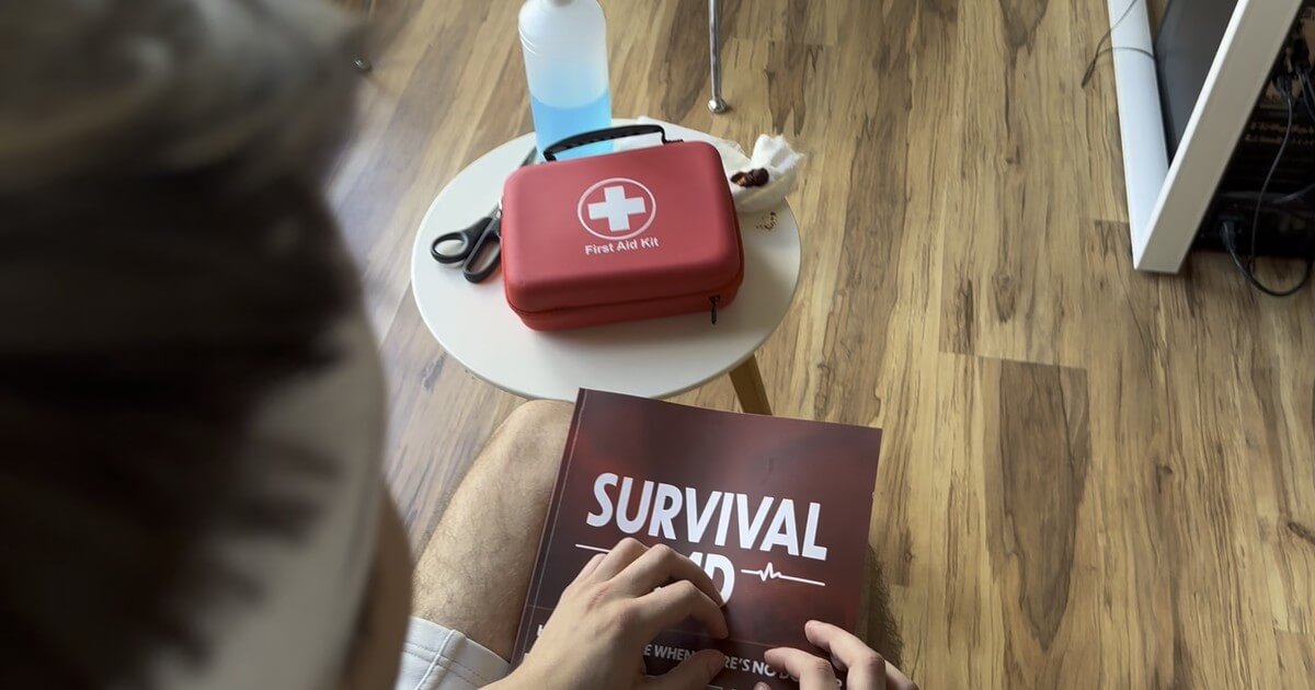 A man with the Survival MD book on his lap and a first aid kit on a side table